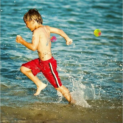 Boy running from reusable water balls being thrown at him at the beach